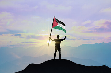 Sudan flag being waved by a man celebrating success at the top of a mountain against sunset or sunrise. Sudan flag for Independence Day.