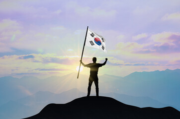 South Korea flag being waved by a man celebrating success at the top of a mountain against sunset or sunrise. South Korea flag for Independence Day.