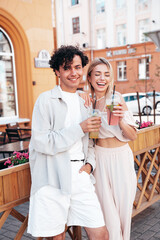 Young smiling beautiful woman and her handsome boyfriend in casual summer clothes. Happy cheerful family. Female having fun. Couple posing in street. Holding and drinking cocktail drink in plastic cup