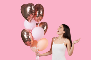 Lady gestures with heart-shaped balloons on pink background