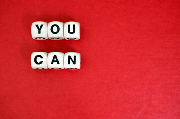 Inspirational mantra You Can spelt with wooden word dice above a red cardboard background.