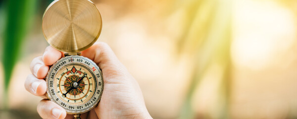 A close-up of a hand grasping a compass in the midst of a lush forest. This image allows for text placement and represents the idea of travel lifestyle and effective business planning and management.