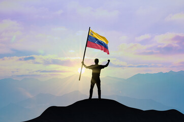 Venezuela flag being waved by a man celebrating success at the top of a mountain against sunset or...