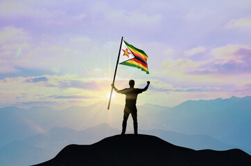 Zimbabwe flag being waved by a man celebrating success at the top of a mountain against sunset or...