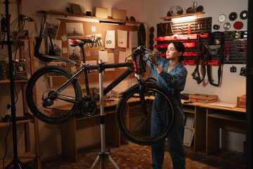 Bicycle female mechanic repairing bicycle doing his professional work in workshop or garage.