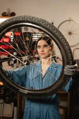 Caucasian young female worker holding and repairing bicycle wheel in bicycle workshop or authentic garage.