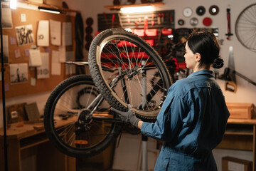 Caucasian young female worker holding and repairing bicycle wheel in bicycle workshop or authentic garage.