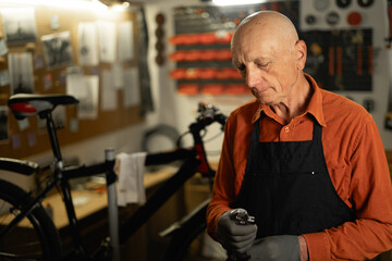 Shot of a old 70s man in his workshop or garage and repairing a bicycle, holding wrench.