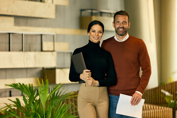 Portrait of two business colleagues, posing for the camera, holding some documents and a laptop. - 781282544