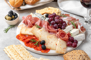 Charcuterie plate with Italian salami and prosciutto ham, with gorgonzrola cheese and pecorino cheese with herbs, served with olives and grapes.  Two glasses of  wine, appetizer platter for aperitif