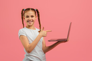 Confident girl holding presenting laptop on pink