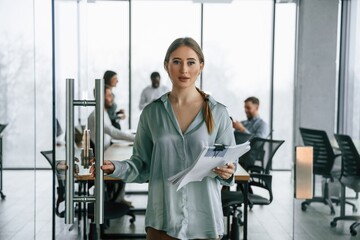 Female manager is with documents. Team of office workers are together indoors