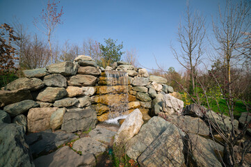 An artificial waterfall with flowing water and stone structures. Authentic landscape overlooking a spring garden.
