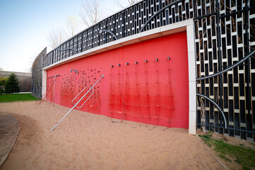 Ropes on the living red wall for active sports, sports equipment in the park. Climbing wall in outdoor. Climbing concrete wall in the park on the street.	