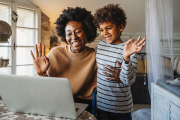 Happy african american single mother and son waving on video call through laptop at home - 781285742