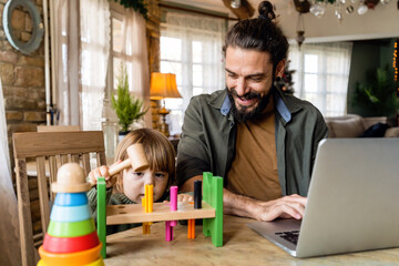 Multi-tasking freelance and fatherhood concept. Working single father with child and laptop computer - 781285990