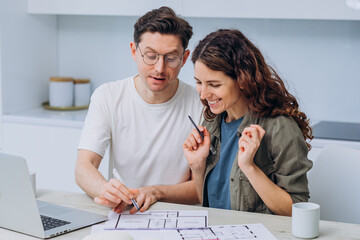 A married couple is planning to renovate an apartment while sitting at a laptop and drawings. The man shows where the living room or children's room will be located. Housewarming, buying a new house.