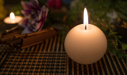 A lit round candle in the foreground and decorative objects in the blurred background. Spa. Dark environment with candlelight in the foreground of the image