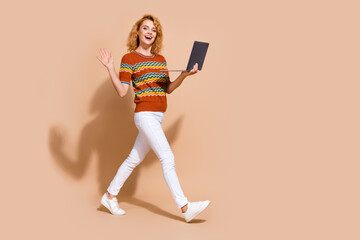 Photo portrait of lovely young lady eshop hold netbook wave hand walking dressed stylish striped garment isolated on beige color background