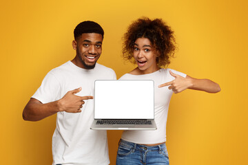 Positive african couple pointing at blank laptop screen