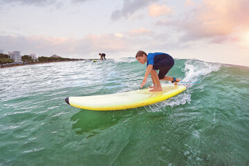 Happy boy take wave in surfing - young surfer learn to ride on surfboard with surf instructor on...