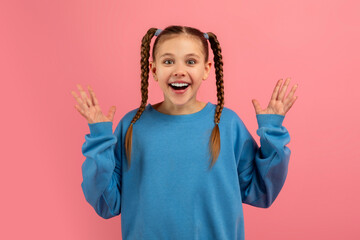 Excited girl with hands up on pink background