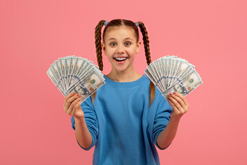 Girl holding money with excited expression on pink background