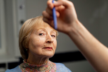 close up In a plastic surgery clinic a doctor makes markings on the face of an elderly woman before...