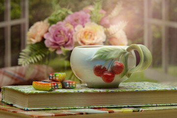 A cup of tea on the windowsill illuminated by the summer sun's rays. Summer still life against the background of a bouquet of flowers on the windowsill. Poster for interior.