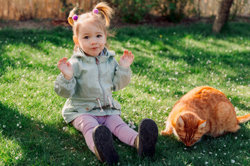 Portrait of child playing with ginger cat in spring backyard garden - 781298730