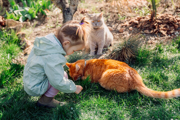 Child girl playing with cats in spring backyard garden