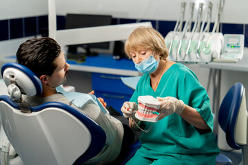 in a dental clinic a dentist shows a patient how to brush his teeth correctly