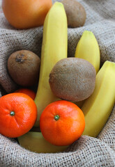 Whole kiwifruits, bananas, mandarins and grapefruit in a fruit basket lined with burlap top view
