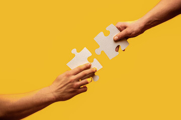 Men holding and putting a piece of jigsaw puzzle together. Two hands trying to connect couple puzzle piece on gray background. Closeup hand of connecting jigsaw puzzle