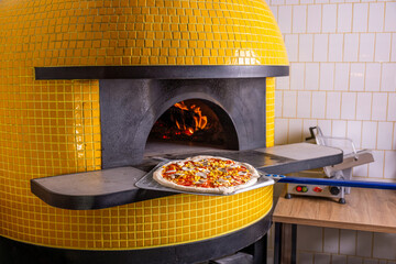 Baked tasty pizza in raditional wood oven in restaurant, Italy. Red hot coal. Italian pizza is cooked in a wood-fired oven. hef holding shovel for pizza,