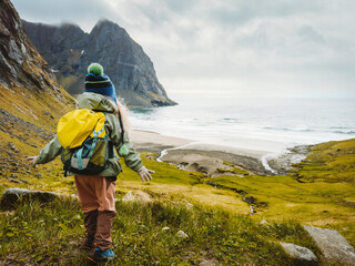 Child traveler hiking to Kvalvika beach in Lofoten islands travel family vacations in Norway outdoor activity healthy lifestyle 4 years old kid with backpack soaking in the ocean view - 781311177