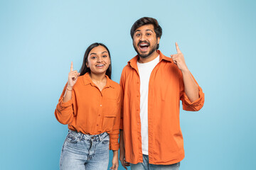 Excited couple pointing upwards together on blue background