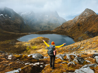 Woman hiking with backpack solo travel in Lofoten islands girl raised hands outdoor in Norway enjoying lake and foggy mountains view, healthy lifestyle active vacations adventure autumn trip