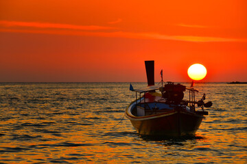 the little wooden fishing boat floating in the sunset sea