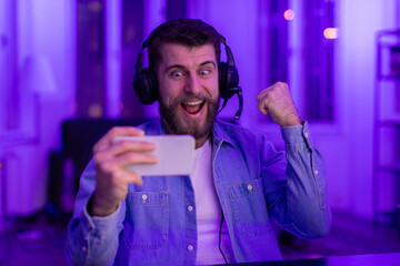 Joyful gamer reacts playing on smartphone in neon light