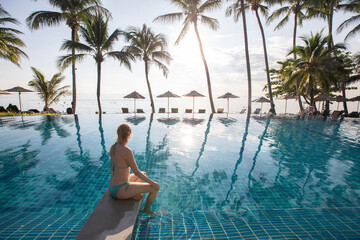 woman in swimsuit sitting near beautiful swimming pool of luxury beach hotel resort
