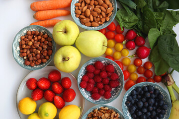 Apples, lemons, bananas, berries, carrots, leek, tomatoes, radishes, spinach and various nuts on white background. Healthy seasonal fruit and vegetable. Top view.