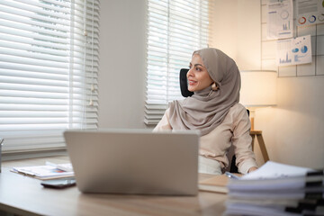 Muslim female entrepreneur wearing hijab sits working with laptop managing personal business in private office.