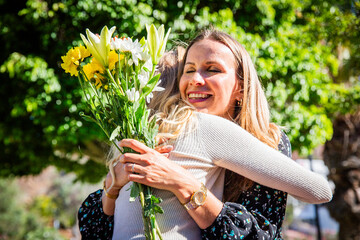 Happy mother hugging her daughter after receiving a bouquet of flowers for mother's day
