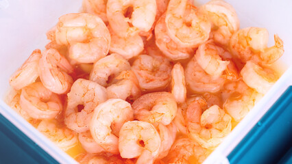 Boiled peeled king prawns in a plastic container on a white background close-up.