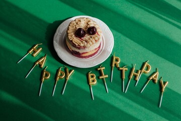 cake on a white saucer, standing on a green background. there are candles nearby for the happy birthday cake - obrazy, fototapety, plakaty