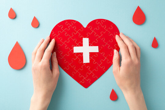 First person top view photo of girl's hands forming heart shaped puzzles with cross sign and blood drops on pastel blue background