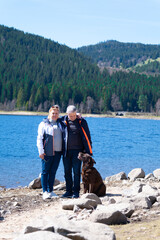 A couple of seniors with dog are staying on the bank near the blue lake