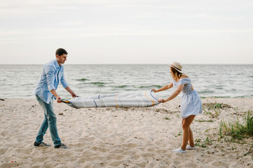 Couple spreading blanket for picnic on sand sea. Happy and funny couple in love on seashore. Female...