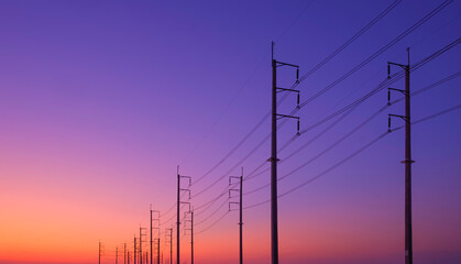 Silhouette two rows of electric poles with cable lines against colorful twilight sky background after sundown, low angle and perspective side view - Powered by Adobe
